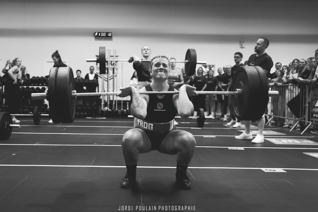Athlète en position basse de front squat avec une barre chargée, pendant une compétition de CrossFit devant le public