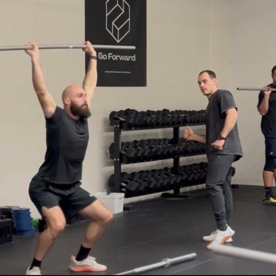 Mathieu, gendarme mobile, en overhead squat à la barre sous l'œil du coach, dans une salle Go Forward